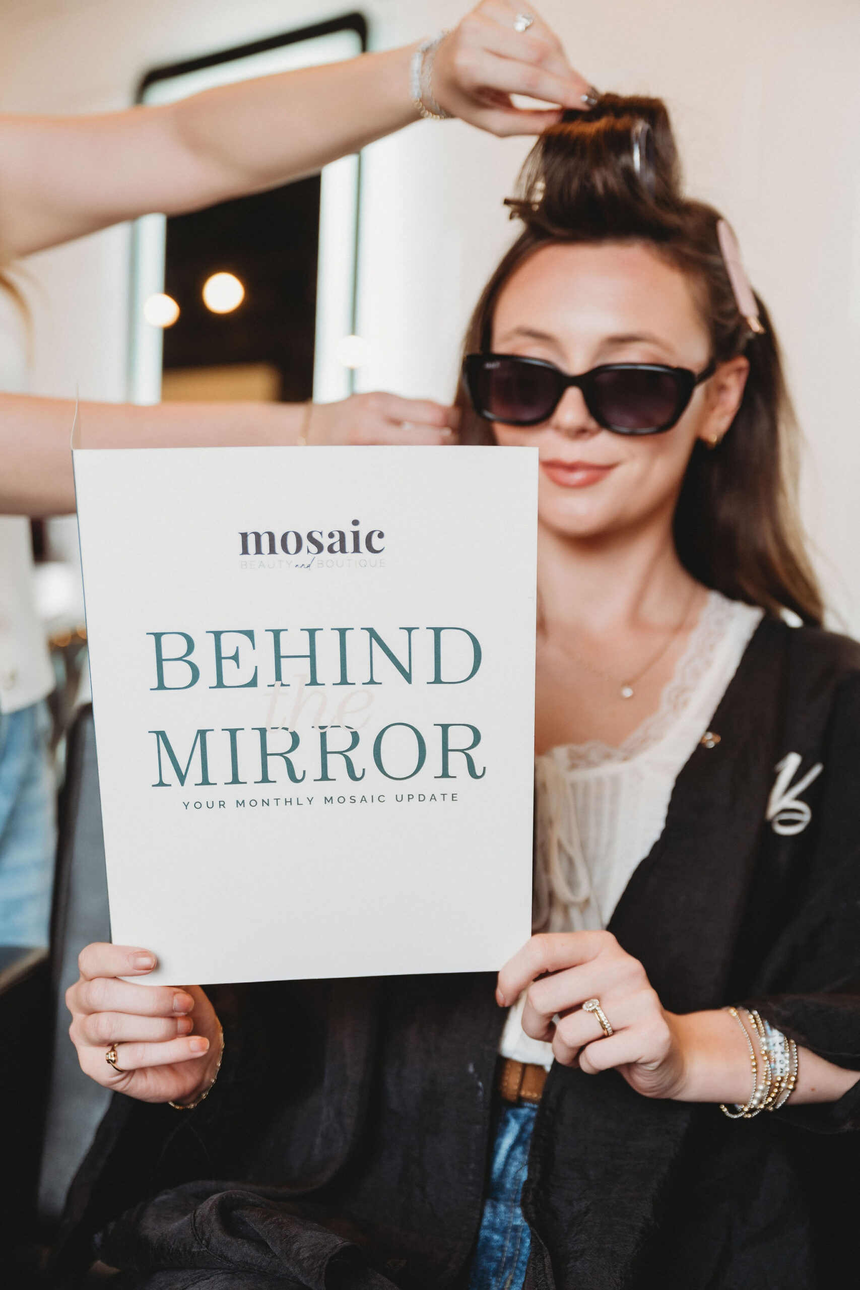 Woman getting her hair styled at Mosaic Beauty & Boutique in Amarillo while holding a Behind the Mirror sign.
